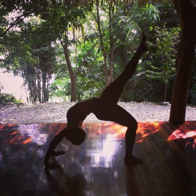 Nicole Spence in wheel pose backbend on yoga mat in natural jungle setting.